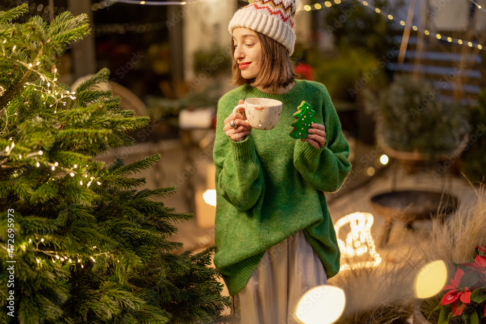 Woman enjoy winter holidays at New Years decorated backyard at night. Cute girl in green sweater an