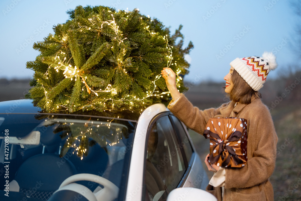 Woman packing Christmas tree on a rooftop of her car, getting ready for a holidays. Idea of Christma