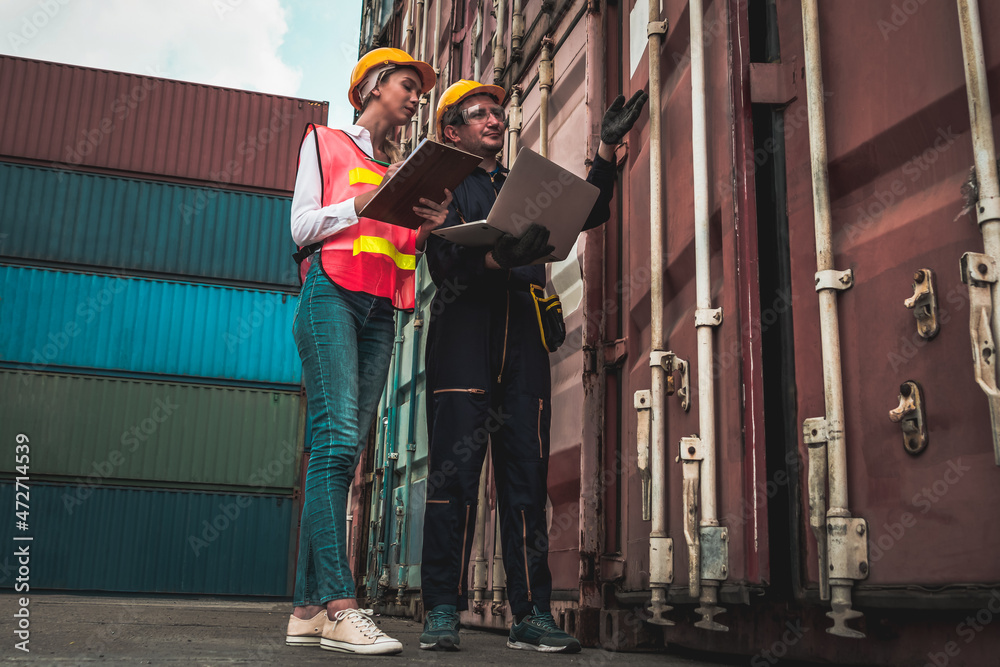 Industrial worker works with co-worker at overseas shipping container yard . Logistics supply chain 