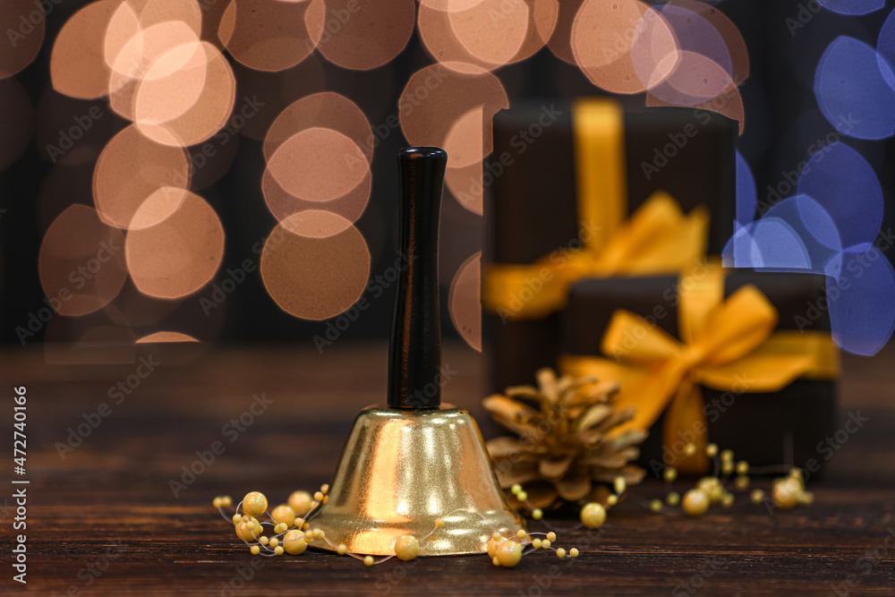 Golden Christmas bell and beads on wooden table against blurred lights