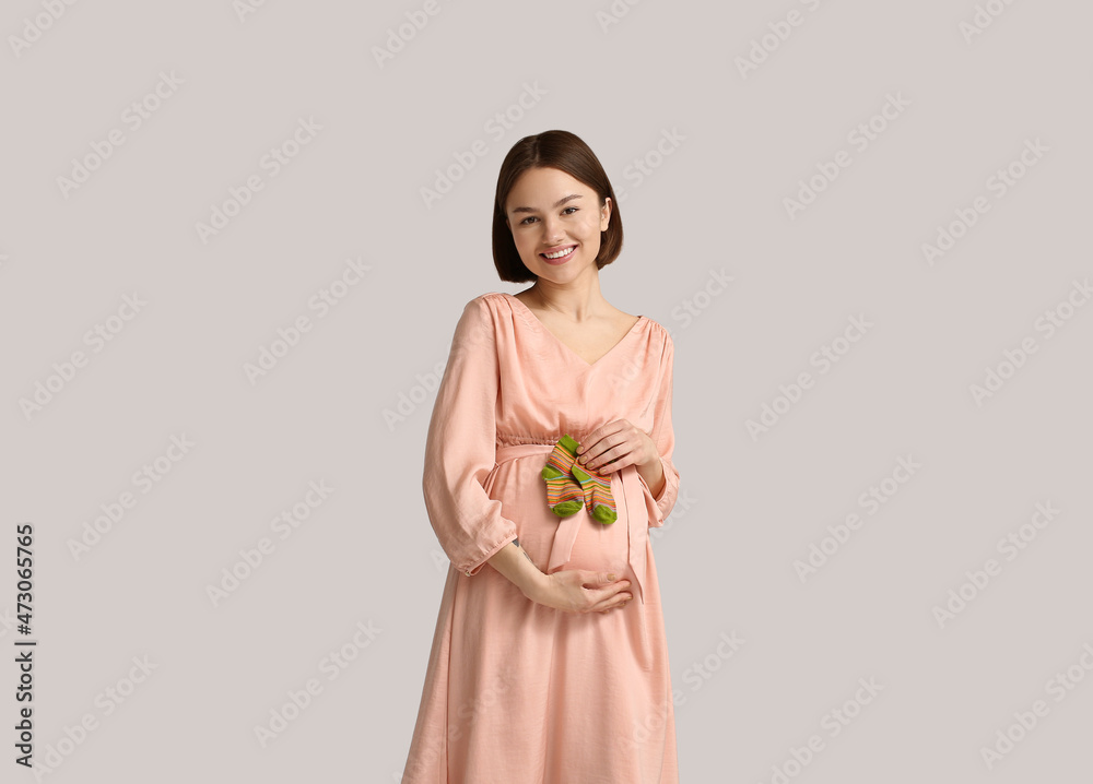 Young pregnant woman with baby socks on light background