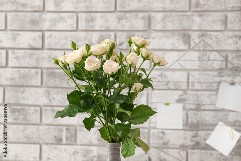 Vase with blooming roses near brick wall