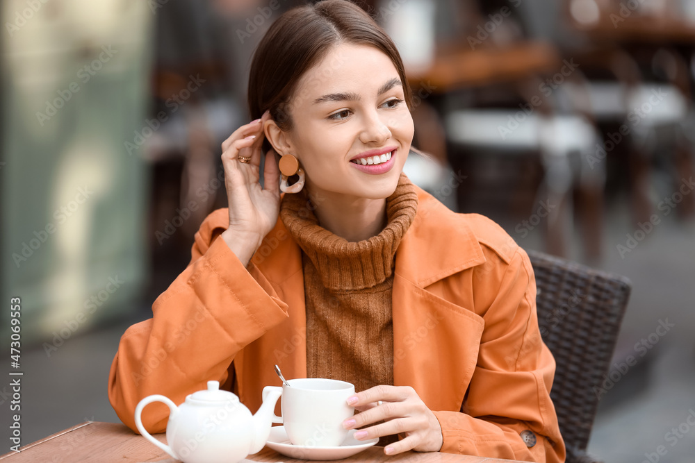 微笑的女人，端着一杯茶，在街头咖啡馆享受秋日