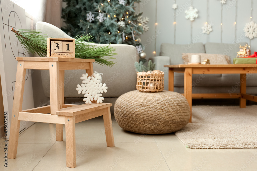 Wooden cube calendar with date DECEMBER 31 and snowflake on wooden stepladder stool in stylish livin