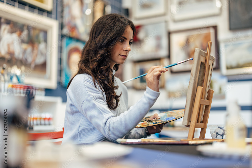 Focused adult woman, working at an art gallery as a painter.