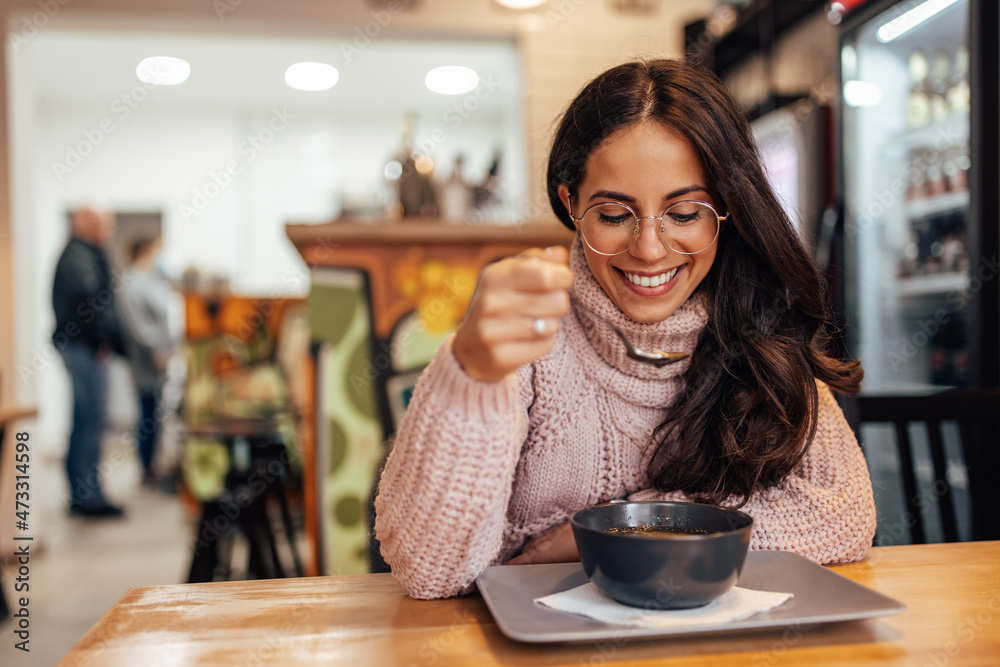 Smiling adult woman, with glasses, waiting for her food to cool.