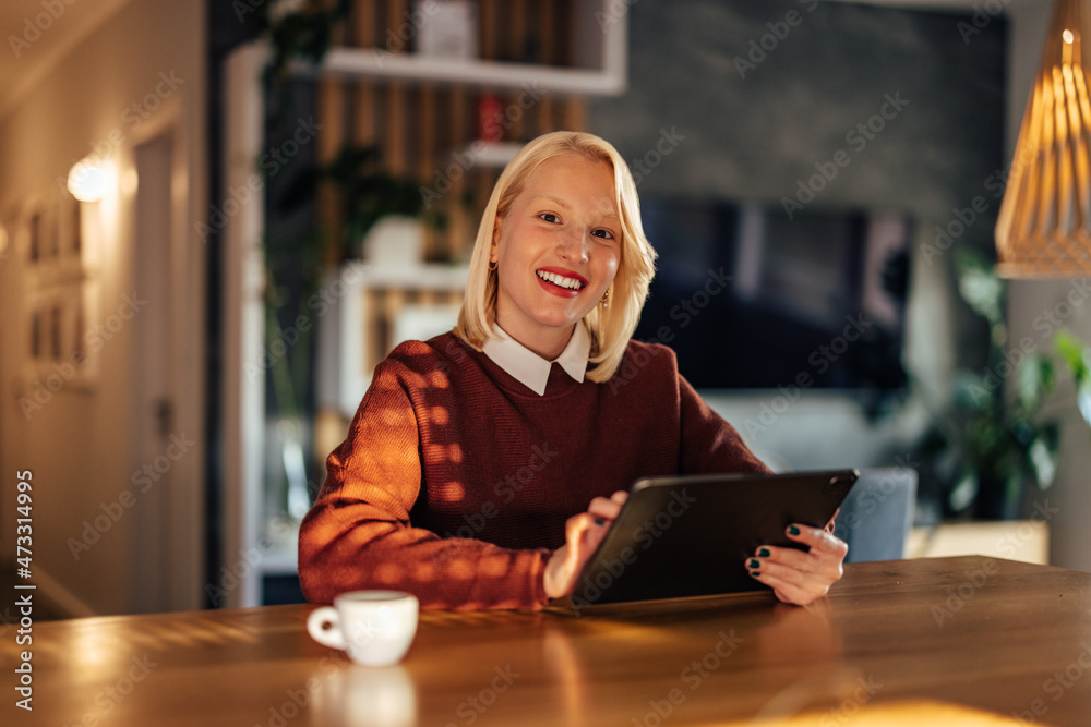 微笑的金发女子在平板电脑上玩电子游戏的肖像。