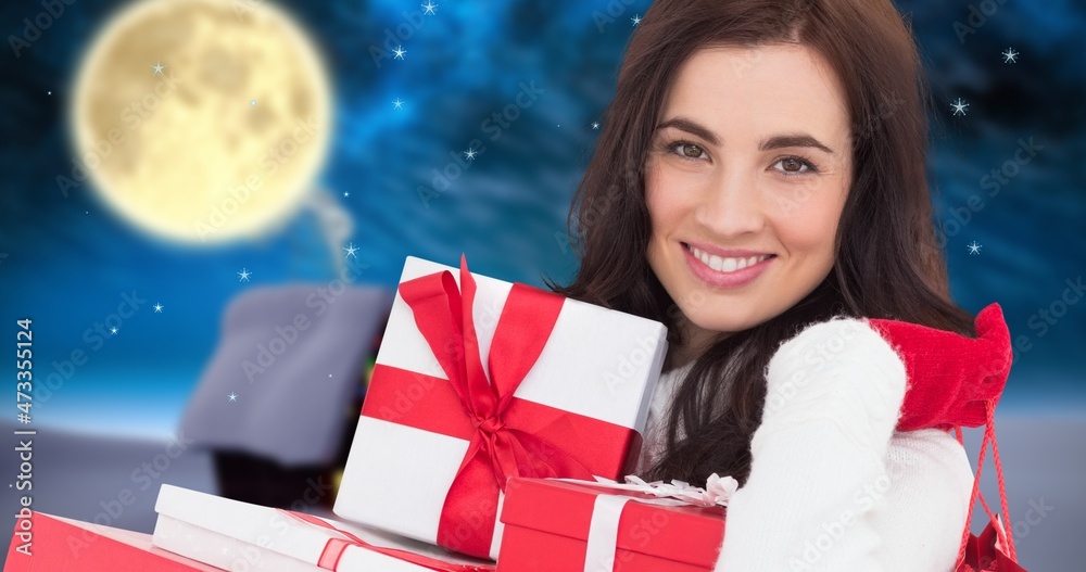 Composition of smiling young woman carrying christmas presents with full moon night in background