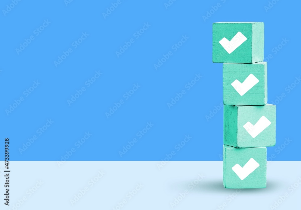 A white checkmarks on a stack of light blue toy blocks on table. Concept of questionary, checklist,