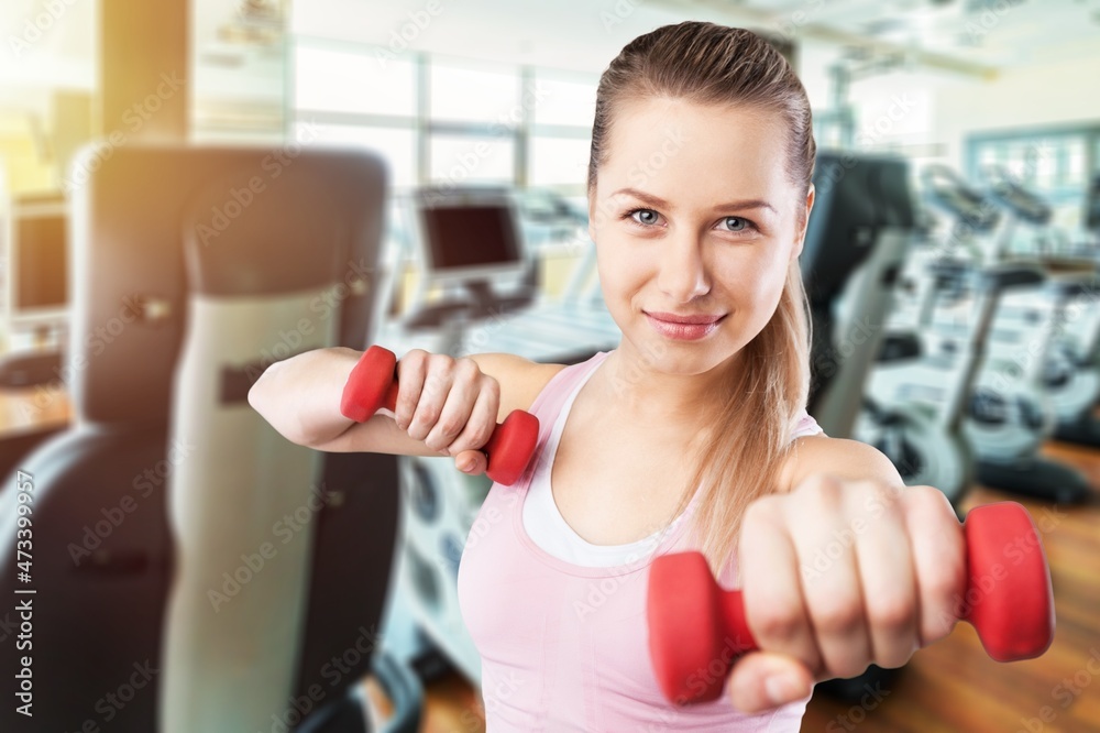 Workout in gym by a beautiful woman using dumbbell. Sport woman warm up before a workout.