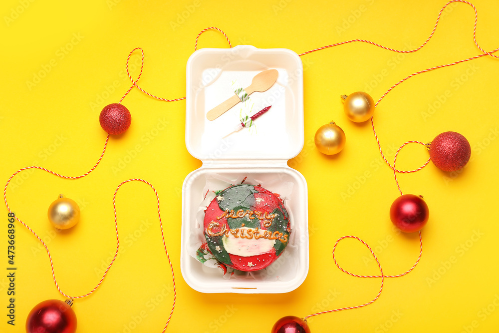 Plastic lunch box with tasty bento cake and Christmas balls on yellow background