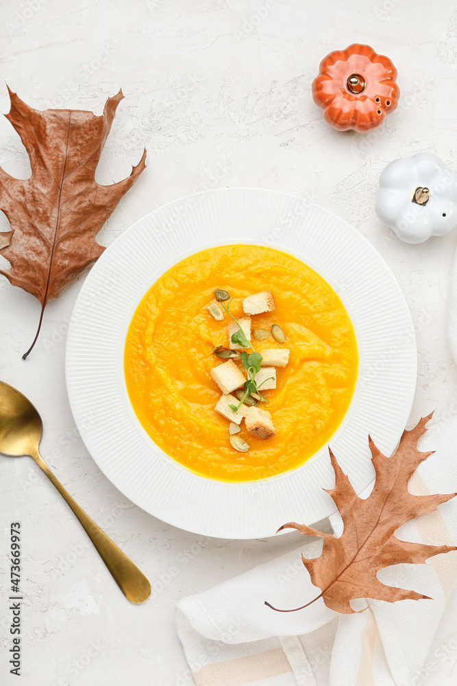 Composition with plate of tasty pumpkin cream soup and autumn leaves on white background