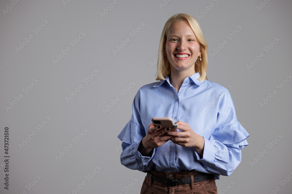 年轻金发女子的肖像，拿着手机对着镜头微笑。