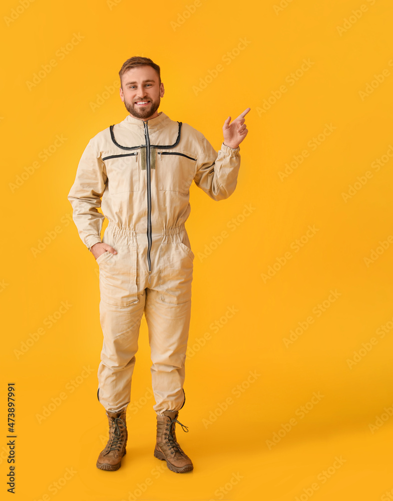 Male beekeeper in protective suit pointing at something on yellow background