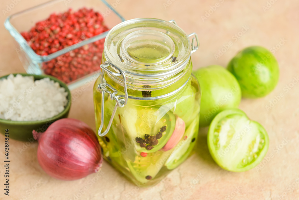 Jar with canned green tomatoes and fresh vegetables on beige background