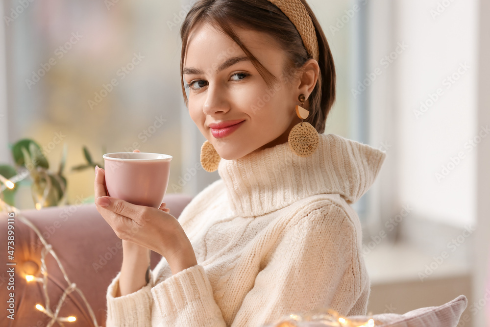 漂亮的年轻女人在家的沙发上喝着美味的茶