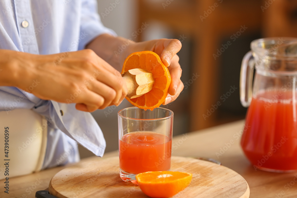 Young woman making fresh citrus juice in kitchen, closeup