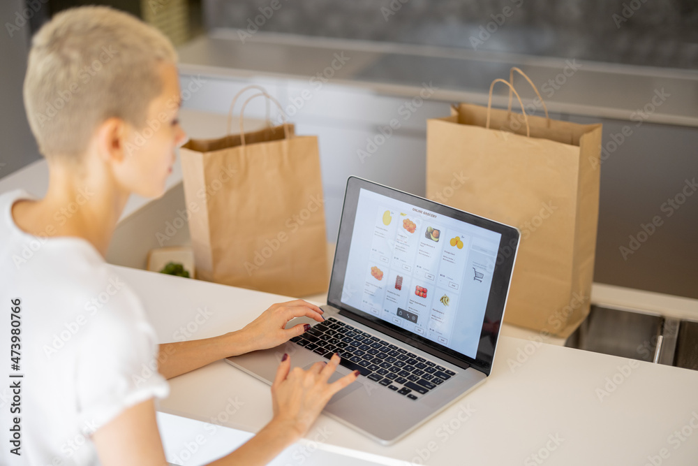 Blonde woman choosing groceries in online store on laptop. Partial of man with shopping bags on back