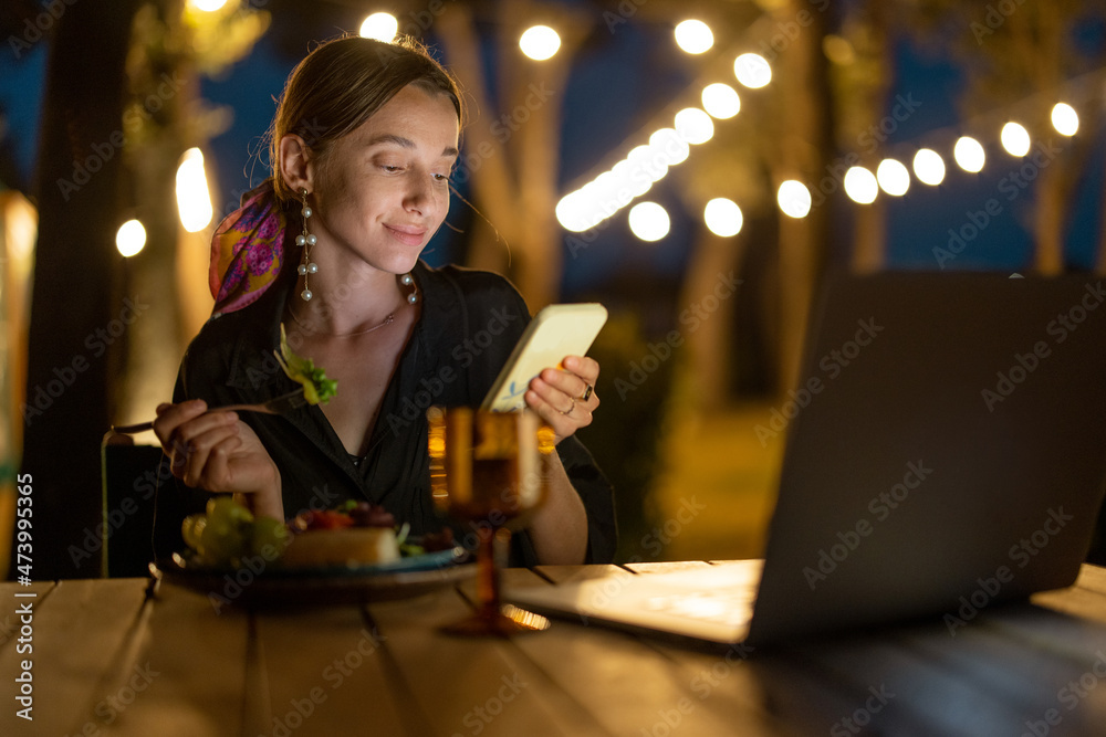 高加索女性晚上在户外用笔记本电脑和手机看东西。年轻女性坐着