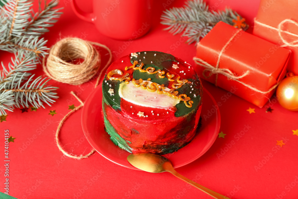 Plate with tasty bento cake and Christmas decor on red background