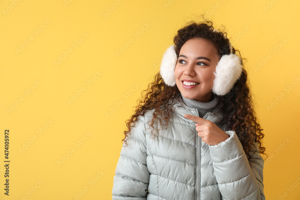 穿着冬装的漂亮非裔美国女人指着彩色背景上的东西