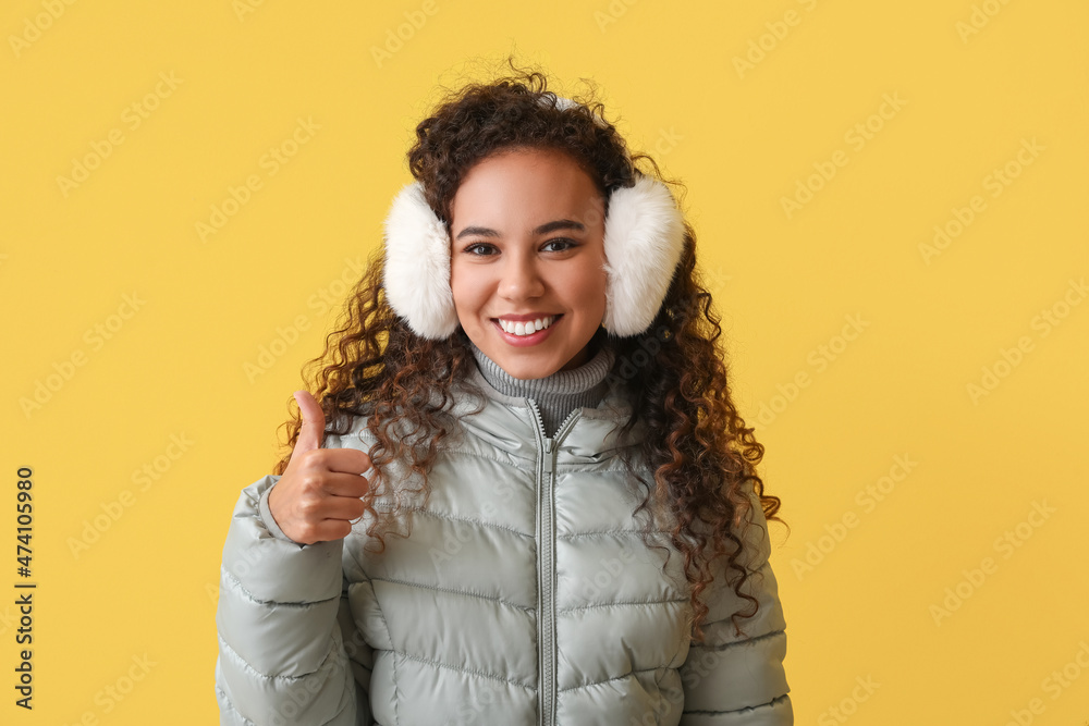 穿着冬装的漂亮非裔美国女人在彩色背景上竖起大拇指