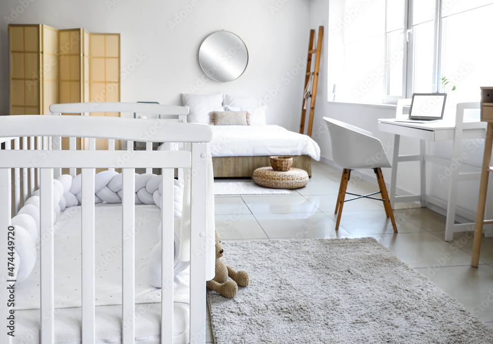 Interior of light bedroom with white crib and modern workplace