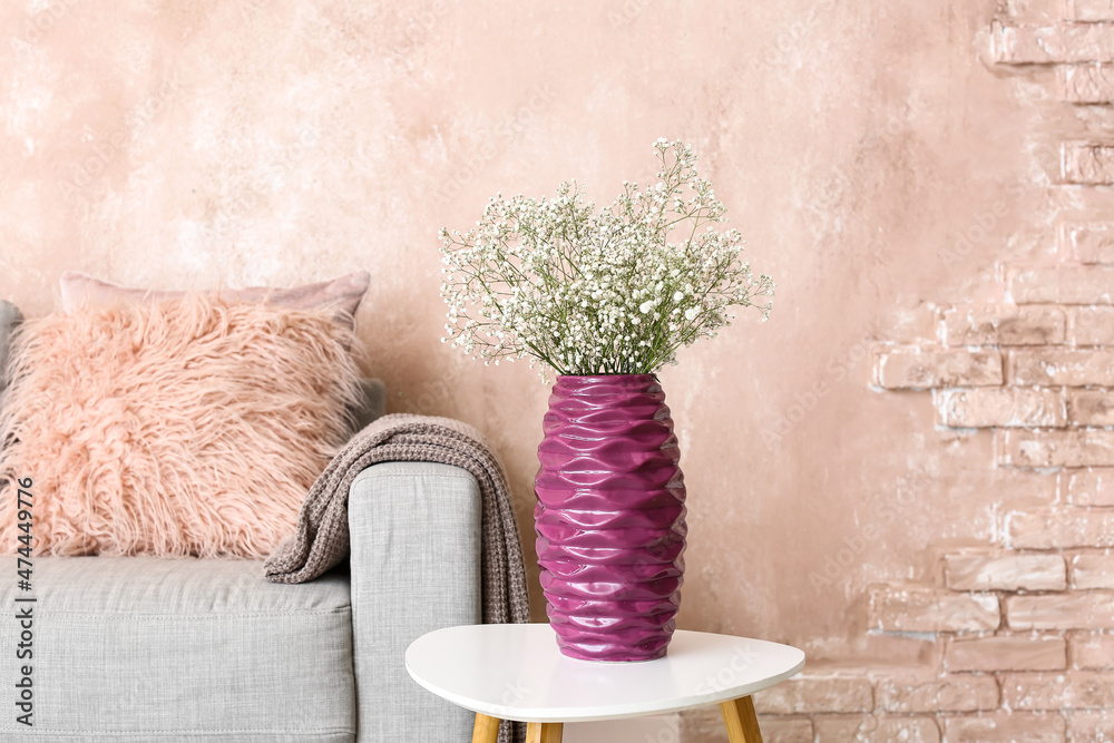 Purple vase with gypsophila flowers on table near pink wall