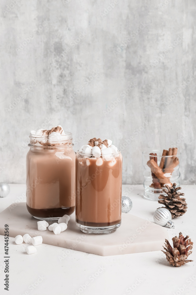 Glass and mason jar of tasty coffee with cinnamon on light background