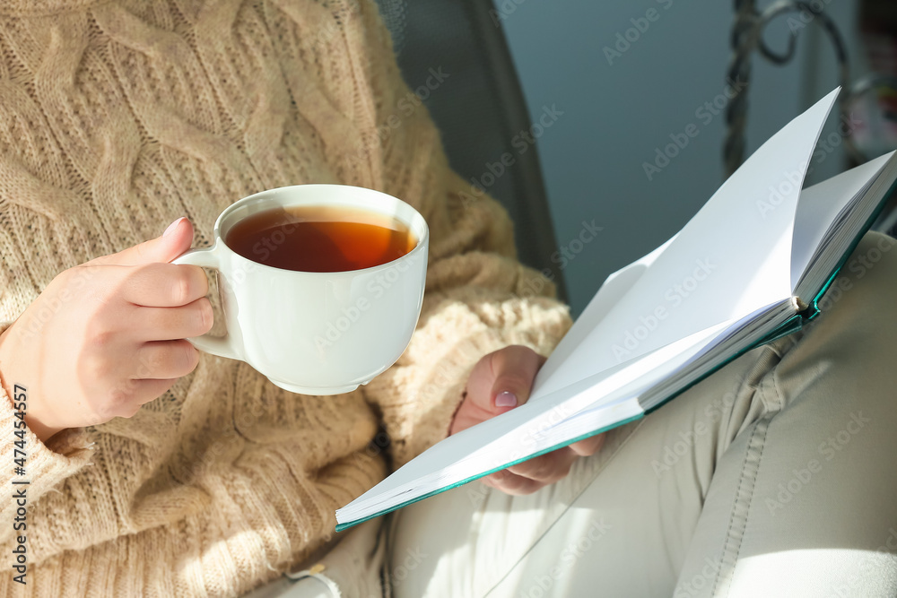 年轻女子拿着一杯美味的茶在房间里看书