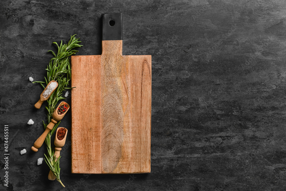 Wooden cutting board and spoons with spices on dark background