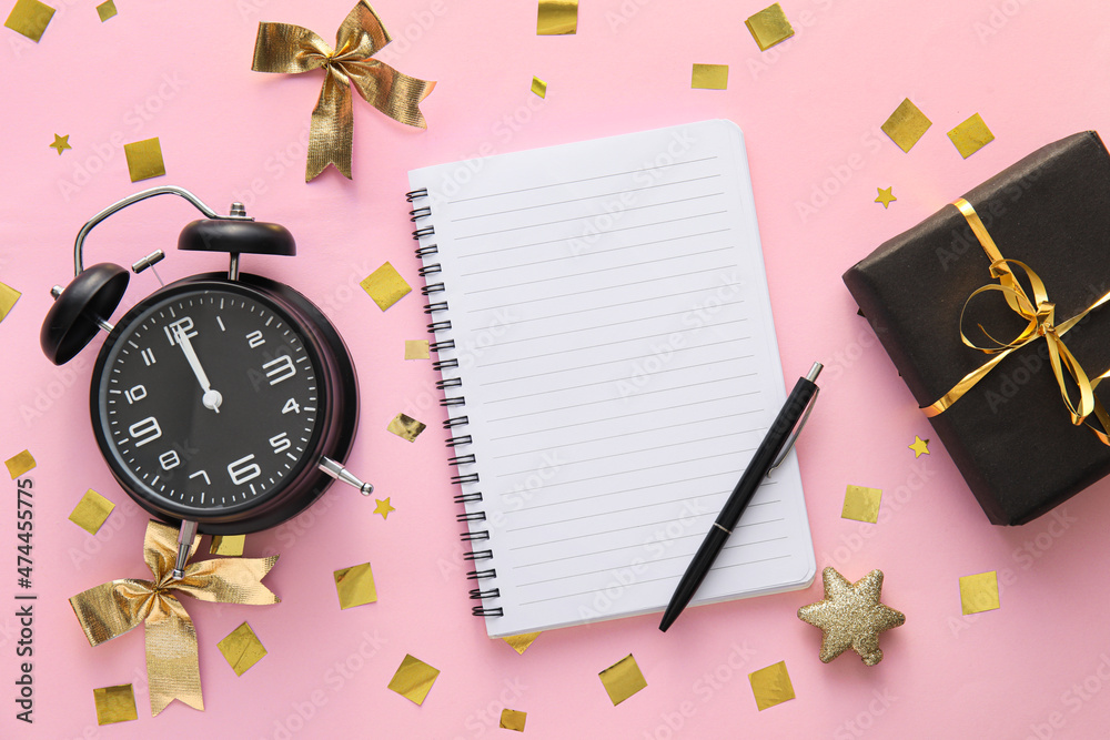 Stylish alarm clock, blank notebook and Christmas decor on pink background