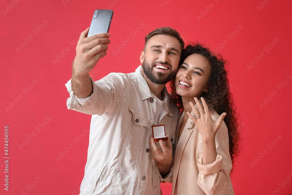 Engaged young couple taking selfie on color background