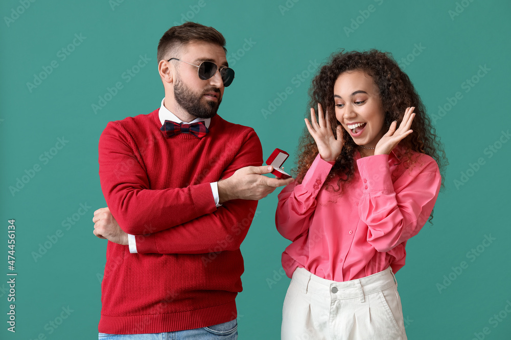 Young man proposing to his girlfriend on color background