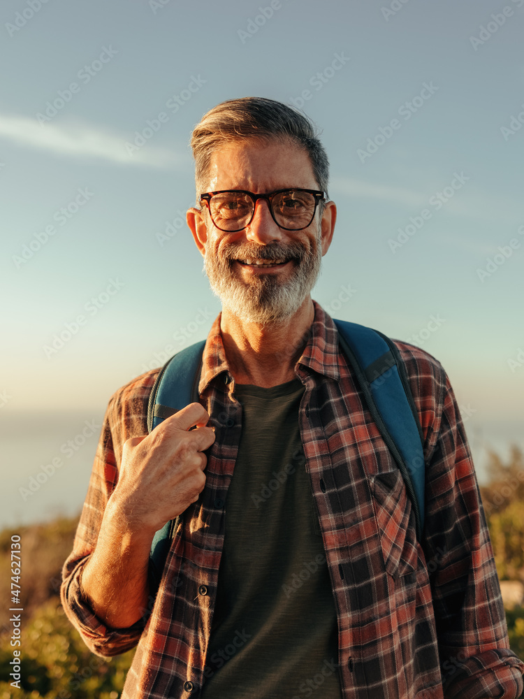 快乐的成熟徒步旅行者站在山顶上对着镜头微笑