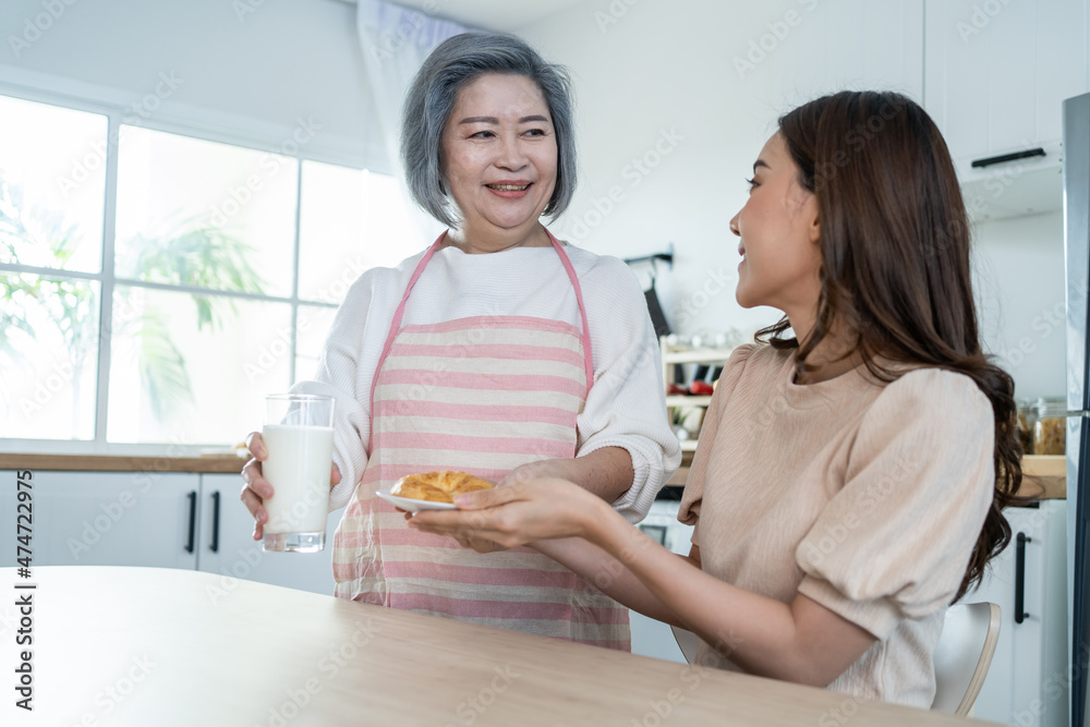 爱亚洲的老年母亲在厨房为女儿提供食物。