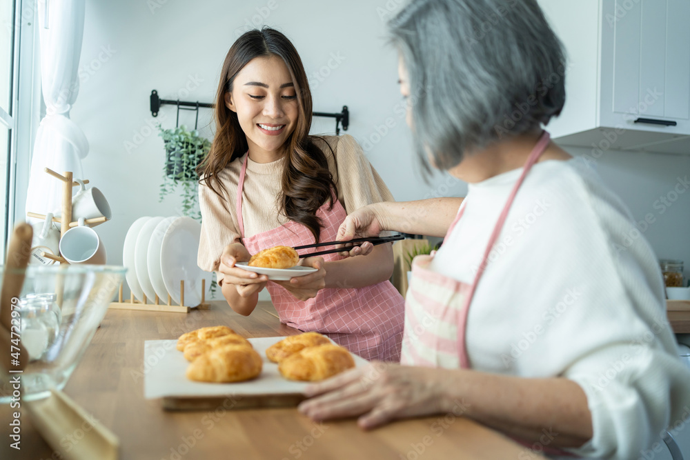 亚洲可爱的家庭，年幼的女儿看着年迈的母亲在厨房做饭