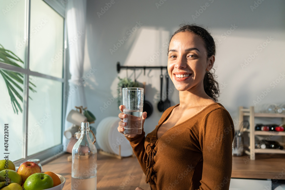 年轻漂亮的拉丁裔妇女在厨房里把干净的水倒入玻璃杯