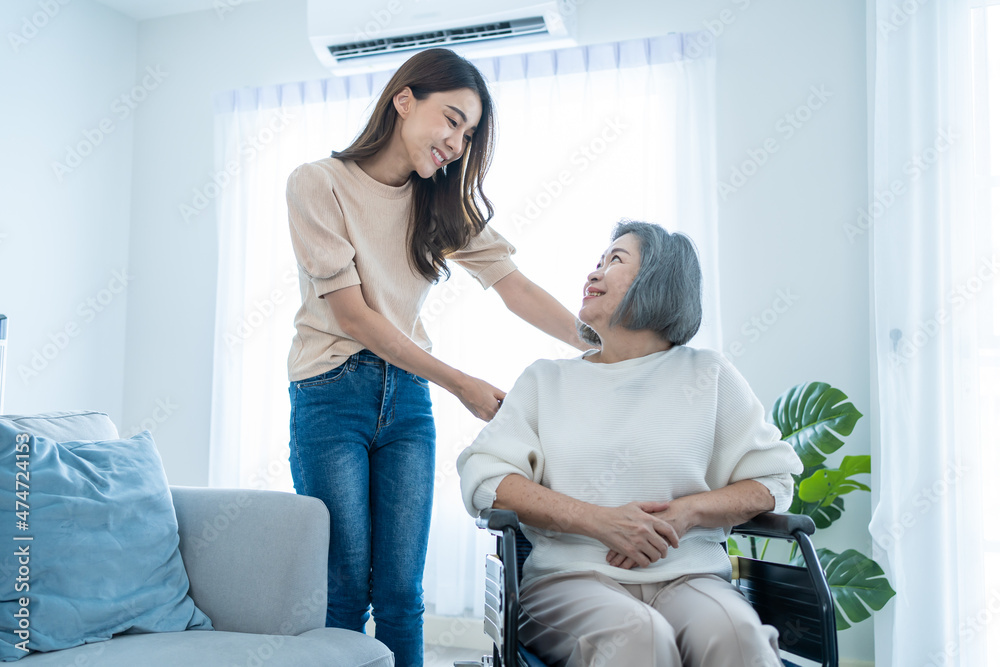 亚洲年轻的女儿在家里支持坐在轮椅上的年长老年妇女。