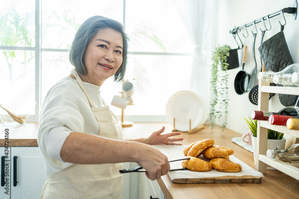 快乐的亚洲老年妇女站在家里的厨房里的肖像。