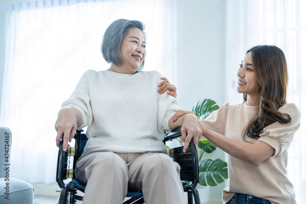 亚洲年轻的女儿在家里支持坐在轮椅上的老年残疾妇女。