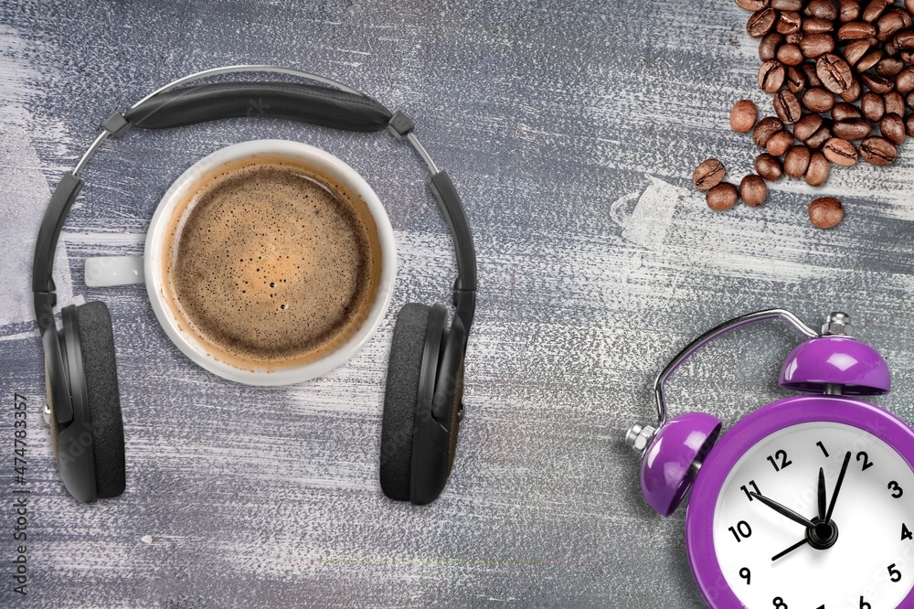 Hot coffee mug with headphones in vintage style and coffee beans on the desk.