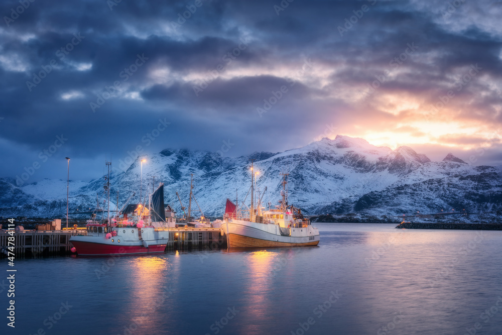 Fishing boats on the sea, snowy mountains, colorful sky with clouds at sunset in Lofoten islands, No