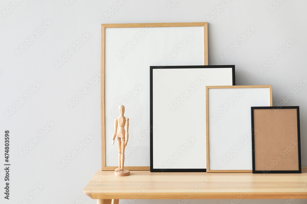 Wooden bench with blank frames and mannequin near light wall