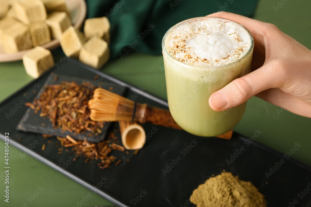 Woman holding glass with tasty hojicha latte on color wooden background, closeup