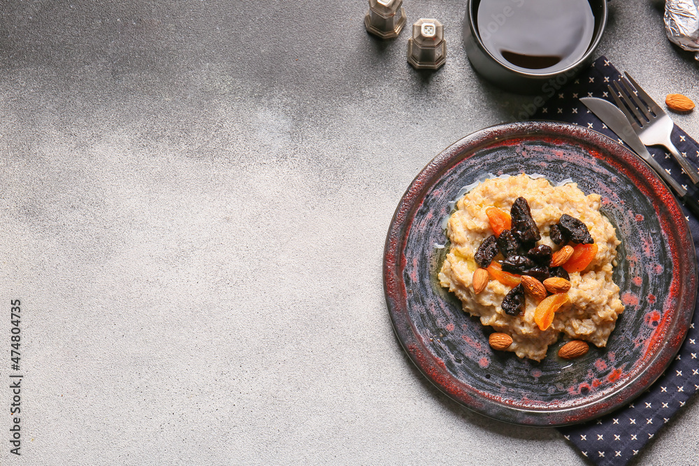 Tasty oatmeal with prunes, dried apricots and almond nuts in plate on grey and white background