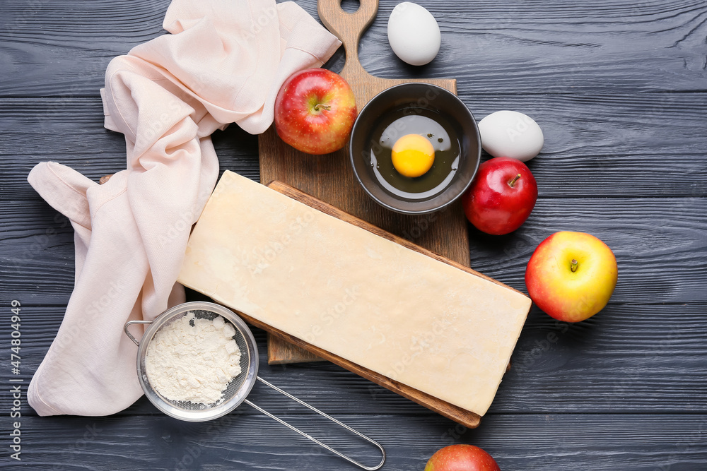 Board with fresh dough and ingredients for apple strudel on black wooden background