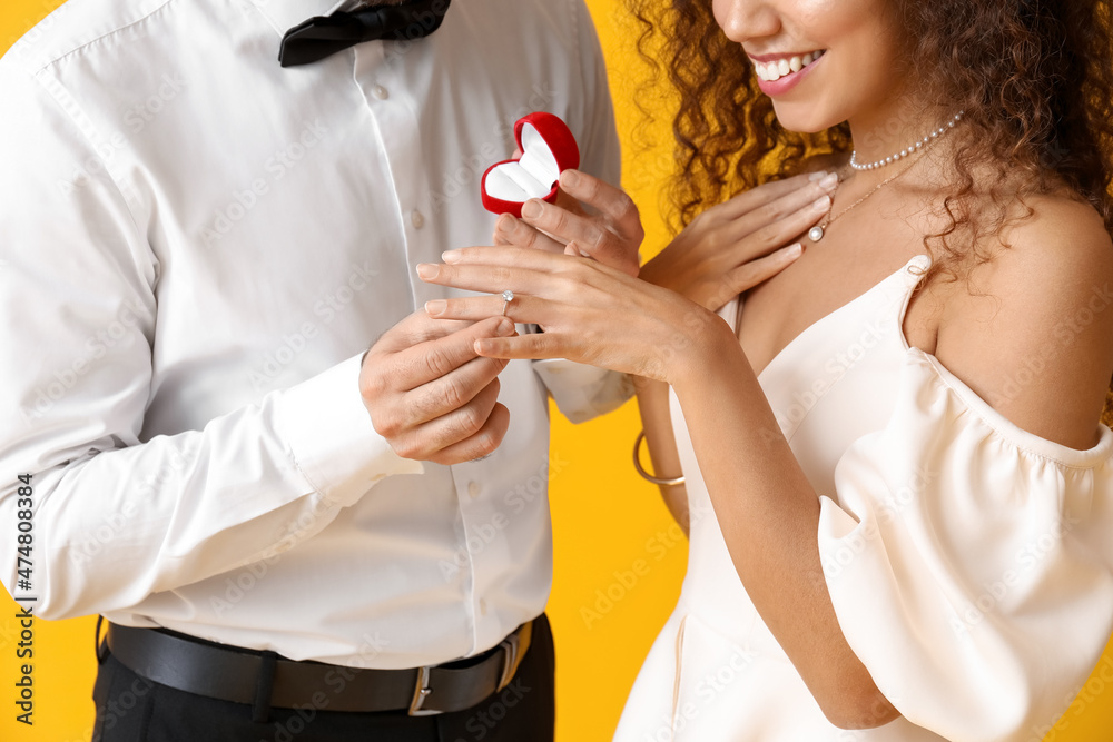 Young man proposing to his girlfriend on color background