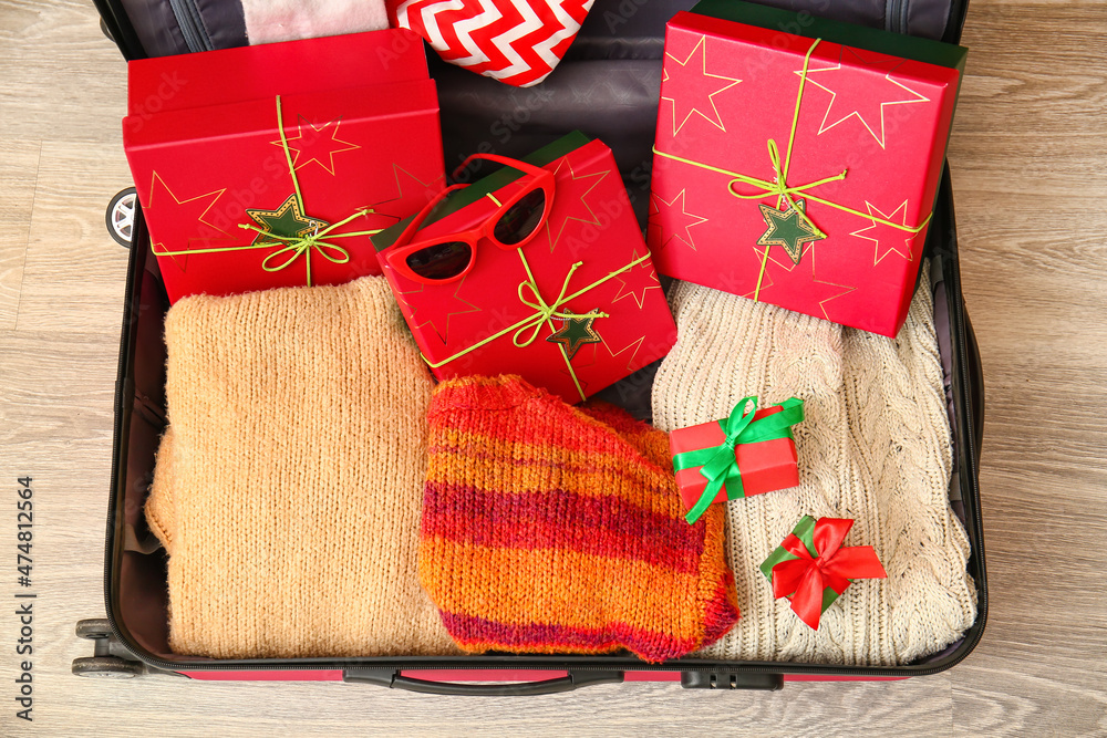 Suitcase with clothes, gift boxes and sunglasses on floor, closeup. Christmas vacation concept