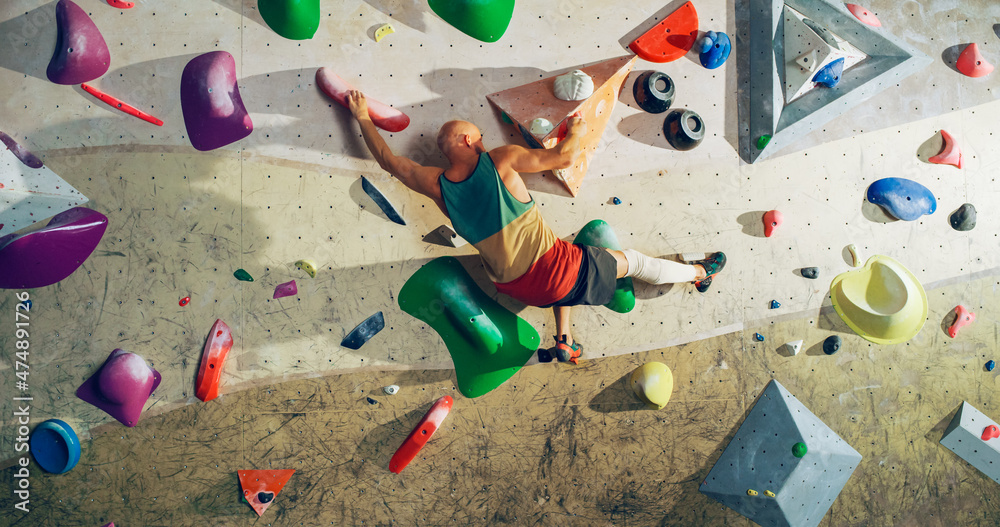 Strong Experienced Rock Climber Practicing Solo Climbing on Bouldering Wall in a Gym. Man Exercising